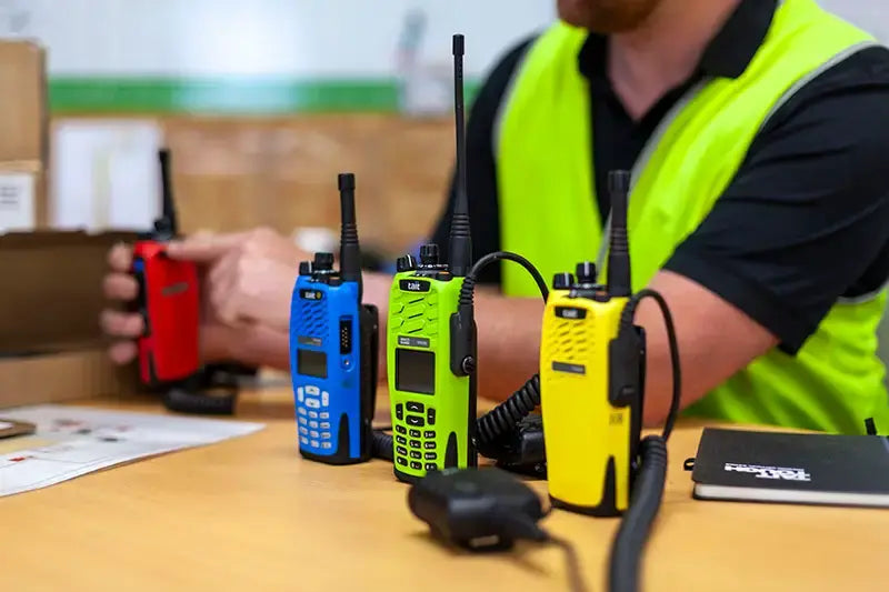 Person wearing a high-visibility vest with walkie-talkies on a table